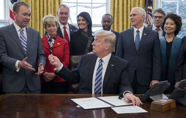 President Donald Trump hands his pen to Mick Mulvaney beside members of his cabinet, including Vice President Mike Pence, in the Oval Office of the White House on March 17, 2017. 