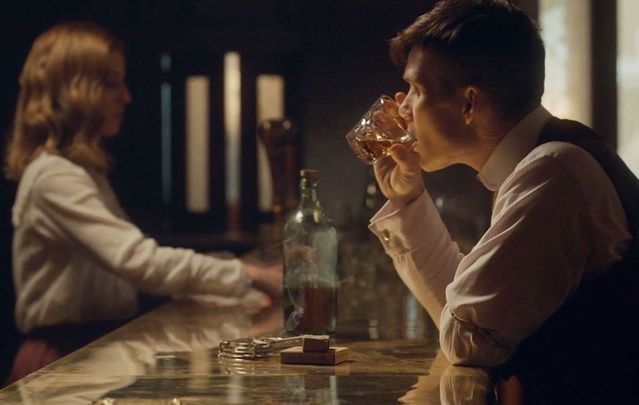 Cillian Murphy, as Tommy Shelby, drinking Irish whiskey in Peaky Blinders. 