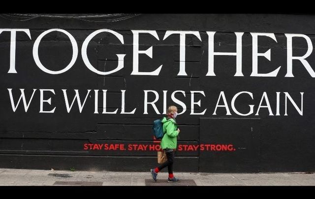 October 19, 2020: A person wearing face masks passes by a mural saying \"Together we will rise again\" on Chancery Street in Dublin.