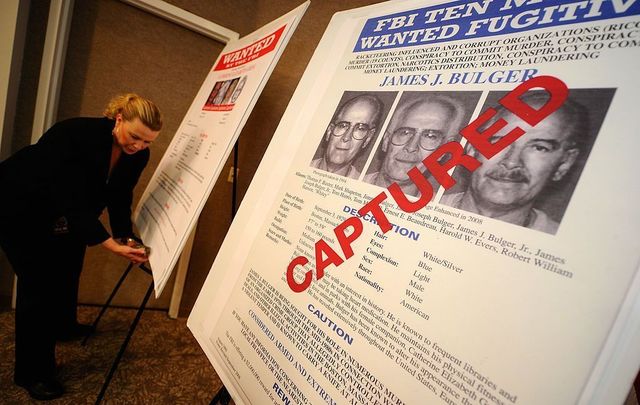 Mary Prang, Special Agent wit the FBI, adjusts a poster featuring fugitives Boston crime boss James \"Whitey\" Bulger.