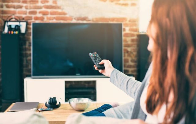 Woman pointing remote at television.