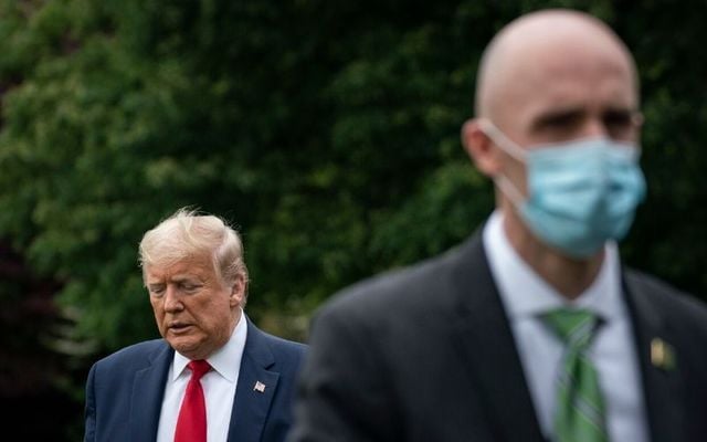 A secret service agent dons a mask while Donald Trump remains maskless. The President has said that he will not order Americans to wear facemasks. 