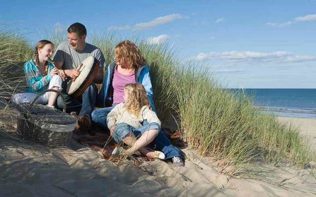 Family picnicking and playing musical instruments on a beach at Brittas Bay, Ireland.