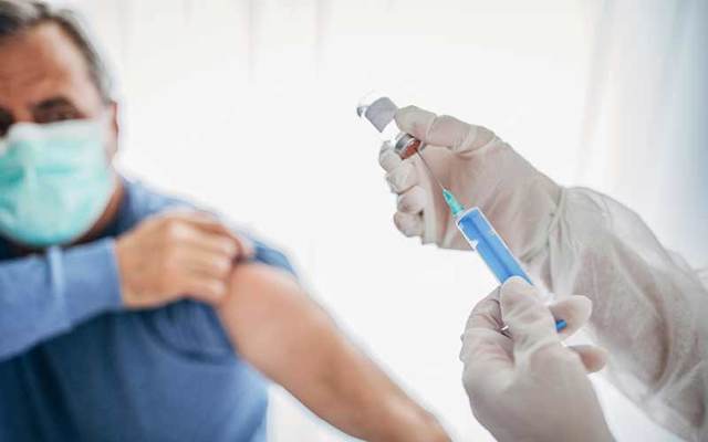 Doctor administers COVID-19 vaccine to masked patient.