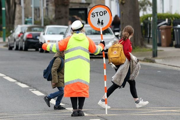 April 12, 2021: Children crossing the road with the help of traffic warden on their way to St Mathews National school in Sandyford, Dublin as all students return to school for the first time. 