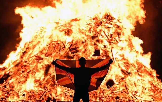 July 11, 2021: A loyalist celebrates with a Union Jack flag as the 11th Night bonfire which marks the beginning of the annual protestant 12th of July celebrations is lit in Portadown, Northern Ireland. 