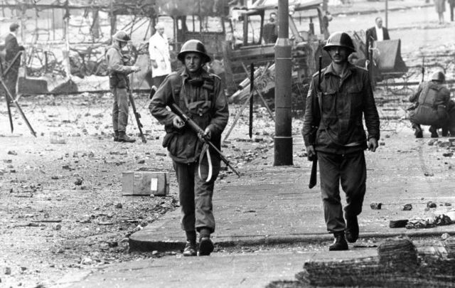 August 16, 1969:  British soldiers on patrol beside barbed wire defences at the junction of Percy Street and Falls Road in Belfast during unrest in Northern Ireland. 
