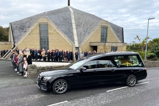 October 12, 2022: Mourners and members of the emergency services waiting outside St. Mary’s Church in Derrybeg as the hearse arrives carrying the coffin for the funeral of Creeslough victim James O\'Flaherty.