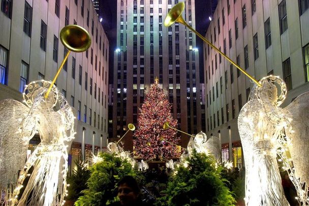 New York City\'s Rockefeller Center plaza, with lit statues of angels and the famous Christmas tree.