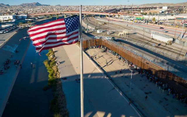 An aerial view of the American flags flying over an international bridge as immigrants line up next to the U.S.-Mexico border fence to seek asylum on December 22, 2022, in El Paso, Texas.