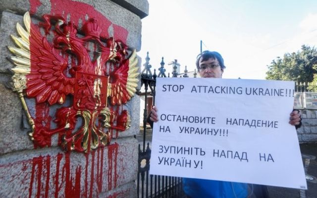 February 24, 2022: Mykhailo Makarov from Ukraine, living in Dublin, protesting outside the Russian Embassy in Dublin. Visible is red paint which was thrown across the coat of arms of the Russian Federation on the gate outside.