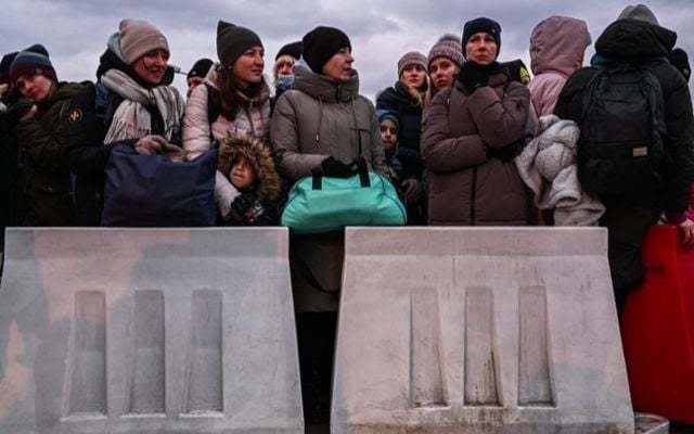 People who fled the war in Ukraine wait in line to board a bus behind removable barriers as Police officers and Polish Territorial defense soldiers help to manage the crowd after crossing the Polish Ukrainian border on March 08, 2022 in Medyka, Poland.