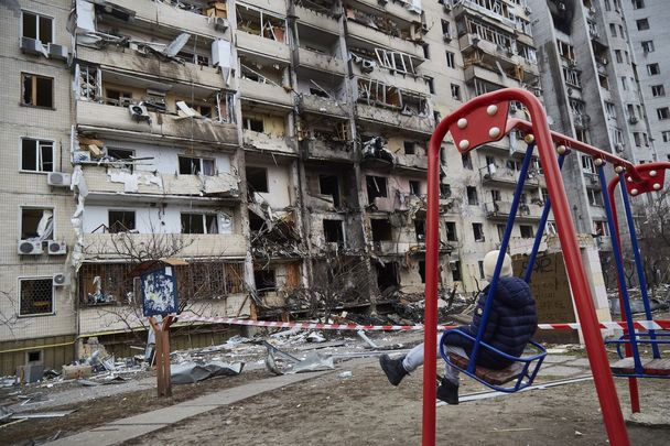 Kyiv, Ukraine: Feb 25, A child on a swing outside a residential building damaged by a missile.
