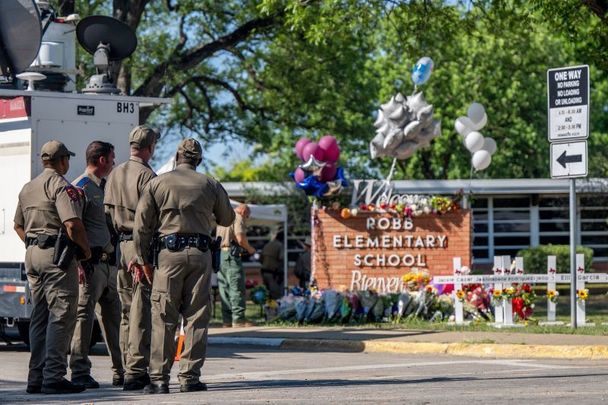 May 26, 2022:  Law enforcement officers stand looking at a memorial following a mass shooting at Robb Elementary School in Uvalde, Texas. 19 students and 2 adults were killed, with the gunman fatally shot by law enforcement.