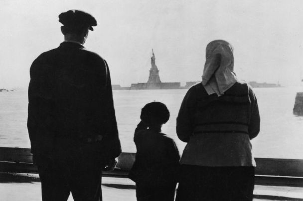 Rear view of an immigrant family on Ellis Island looking across New York Harbor at the Statue of Liberty, 1930s.