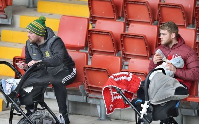 Two men tending to their children while their wives play camogie.
