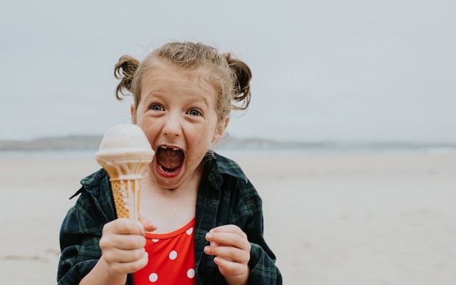 July 16 is National Ice Cream Day. A little girl stands on a beach holding an ice cream cone with an excited look on her face.