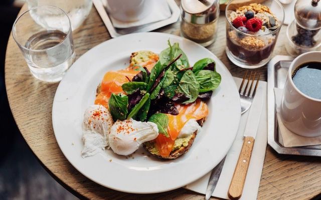 A healthy breakfast of avocado toast, salmon, spinach and poached egg with coffee and muesli.