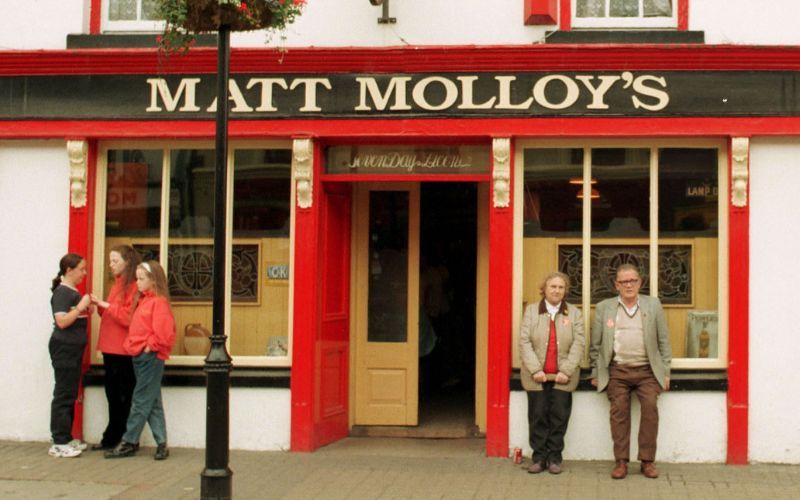 Matt Molloy in aighneas faoi phlean do bhrú (hostel) in aice lena theach tábhairne (pub)
