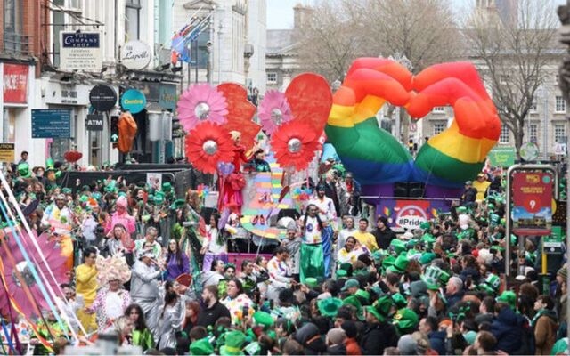 The 2025 St. Patrick\'s Day Parade moves through Dublin, along Dame Street, looking back at Trinity College.