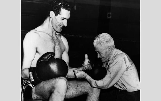 18th March 1948: Tall Irish boxer Jim Cully, 7ft 2ins, from Tipperary smiles as a US boxing authority, \'Pop\' Gleason, attempts to put a regulation-sized glove on his big hand.
