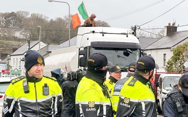 April 10, 2026: A protestor with an Irish flag stands on top of a tanker behind a standoff between members of the Garda Public Order Unit and protestors outside the Irving Oil Refinery in Whitegate, Co Cork.