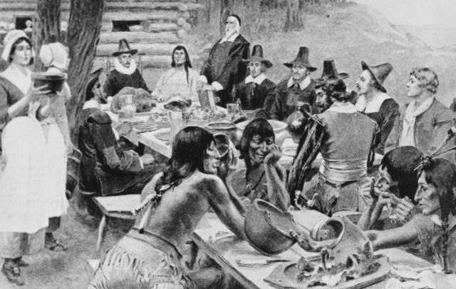 A depiction of early settlers of the Plymouth Colony sharing a harvest Thanksgiving meal with members of the local Wampanoag tribe at the Plymouth Plantation, Plymouth, Massachusetts, 1621.