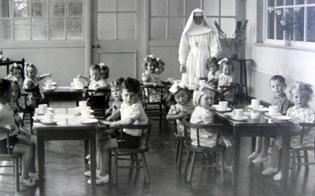 The horrors of Mother and Baby Homes. Children sit in a tea room with a nun posing for a photo.