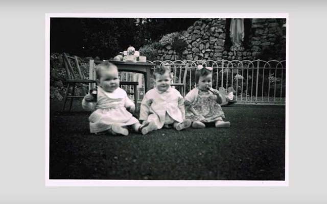 Black-and-white photograph of three infants sitting on a lawn.