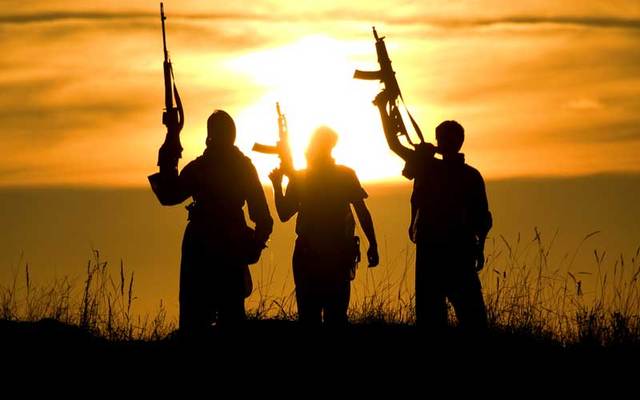 A group of jihadis raise their weapons against the setting sun.