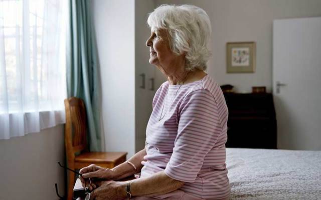 An older woman sitting in solitude looking out a window.