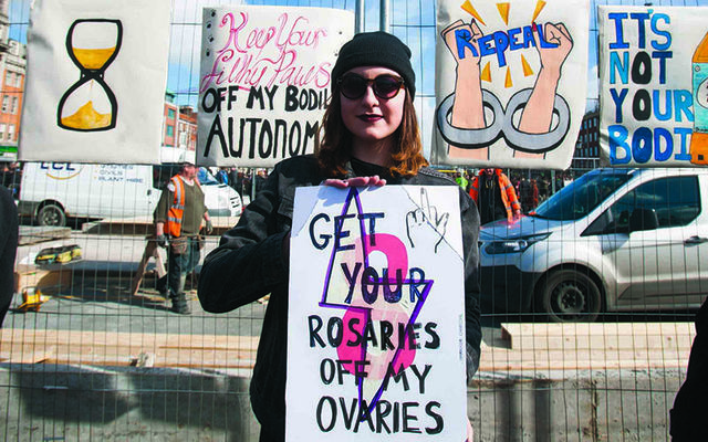 A pro-choice protester at a Strike for Repeal event with a sign reading \"get your rosaries off my ovaries\".