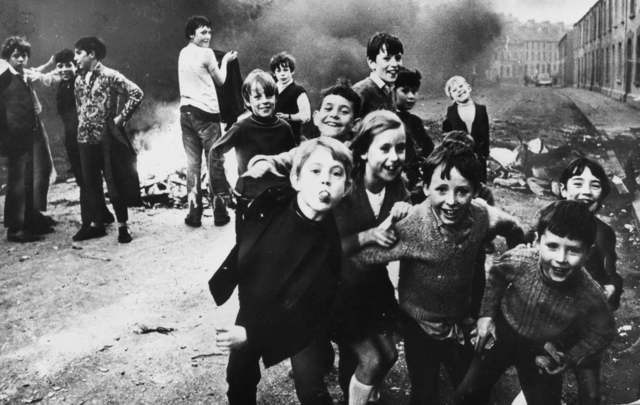7th December 1971: Children jeer at British soldiers while a fire smolders in the street behind them.