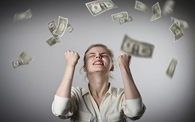 A woman stands under money falling from the sky.