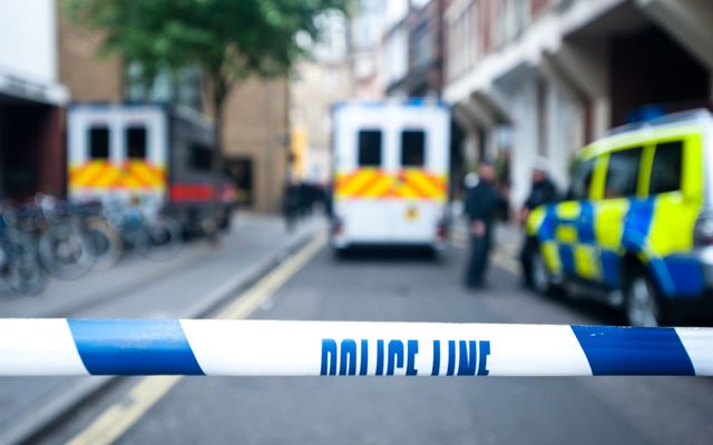 Police officers and vans behind safety police line tape.\n