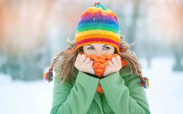 A young woman in the snow with a scarf on her face trying to warm herself.