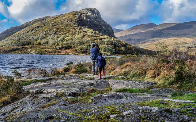 A family with a dad and young daughters looks out to an idyllic and incredible view in Killarney, Ireland. 