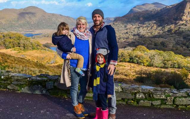 A snap of a young family with two children posing in front of Lady\'s View, a scenic and beautiful valley in Ireland, within the Ring of Kerry. \n
