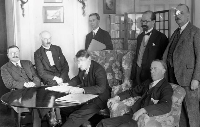 The signing of the Irish Free State Treaty in London, December 6, 1921. From left: Arthur Griffith, Eamon Duggan, Michael Collins, Robert Barton. Standing from left: Robert Erskine Childers, George Gavan Dufy, and John Chartres