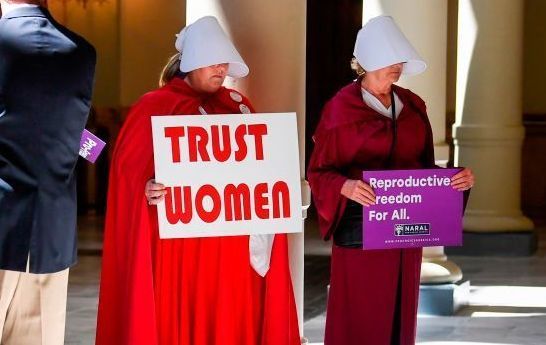 Activist Tamara Stevens (L) with the Handmaids Coalition of Georgia holds a sign as Democratic presidential candidate Sen. Kirsten Gillibrand (D-NY) addresses an event at the Georgia State Capitol to speak out against the recently passed \"heartbeat\" bill on May 16, 2019, in Atlanta, Georgia. 