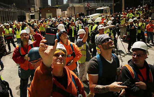 Construction workers watch as the final two sections of a 408-foot spire are placed on a temporary platform on the top of One World Trade Center