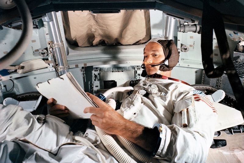 June 16, 1969: Michael Collins laying down, observing a checklist in a simulator of the command module. (Public Domain / NASA)