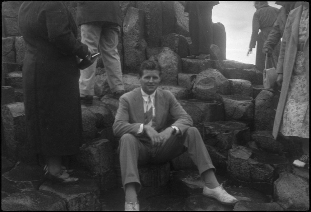 Joseph P. Kennedy, Jr. (center, surrounded by several unidentified people), sits on the basalt rock at Giant's Causeway in Bushmills, Northern Ireland, during a Kennedy family trip in 1937. Original caption read "Joe, Giants Causeway." Photographer unknown. Copyright John F. Kennedy Library Foundation. Kennedy Family Collection. John F. Kennedy Presidential Library and Museum, Boston