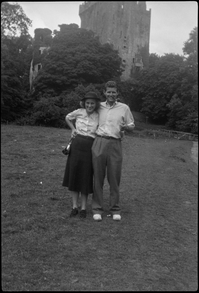 Kathleen Kennedy (wearing hat) and Joseph P. Kennedy, Jr. (smoking a pipe), stand on the grass with their arms around each other outside Blarney Castle in Blarney, Ireland, during a Kennedy family trip. Photographer unknown. Copyright John F. Kennedy Library Foundation. Kennedy Family Collection. John F. Kennedy Presidential Library and Museum, Boston