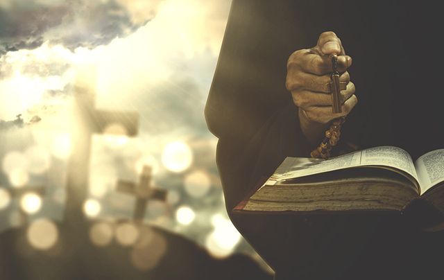 Priest holding Rosary over a Bible. Credit: iStock