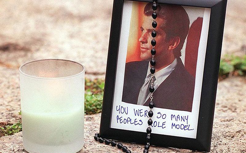 A candle, rosary beads and a photo of John F. Kennedy Jr adorn the gravesite of his father, assassinated US President John F. Kennedy 21 July 1999, at Arlington National Cemetery. Image: JOYCE NALTCHAYAN/AFP/Getty Images.