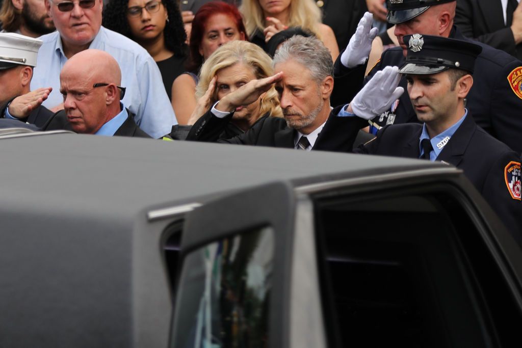 Comedian and activist Jon Stewart (C) and U.S. Rep. Carolyn Maloney (D-NY) (C-L) salute the casket of retired NYPD detective Luis Alvarez as it is brought into Immaculate Conception Church on July 03, 2019 in the Queens borough of New York City. (Photo by Spencer Platt/Getty Images)
