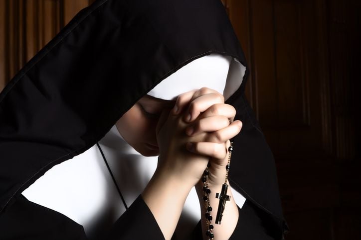 A nun holding a rosary praying. Credit: Getty Images/Studio-Annika