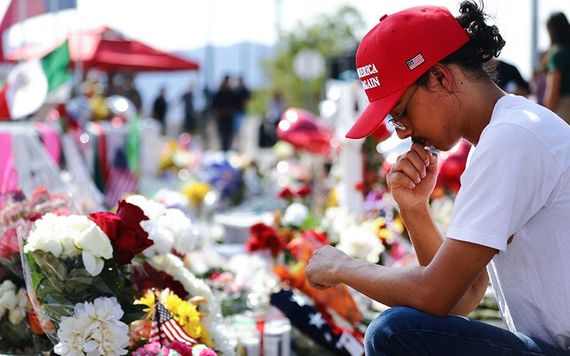 A man wearing a Donald Trump "Make America Great Again" kneeling before a memorial in El Paso.