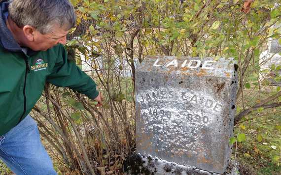 Mike holding shrubs back from gravestone of his second great grandfather James Laide. The gravestone was “lost in time” before being rediscovered by Kate.